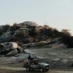 A vintage jeep drives through a rocky landscape during the day, capturing adventure and rugged terrain.
